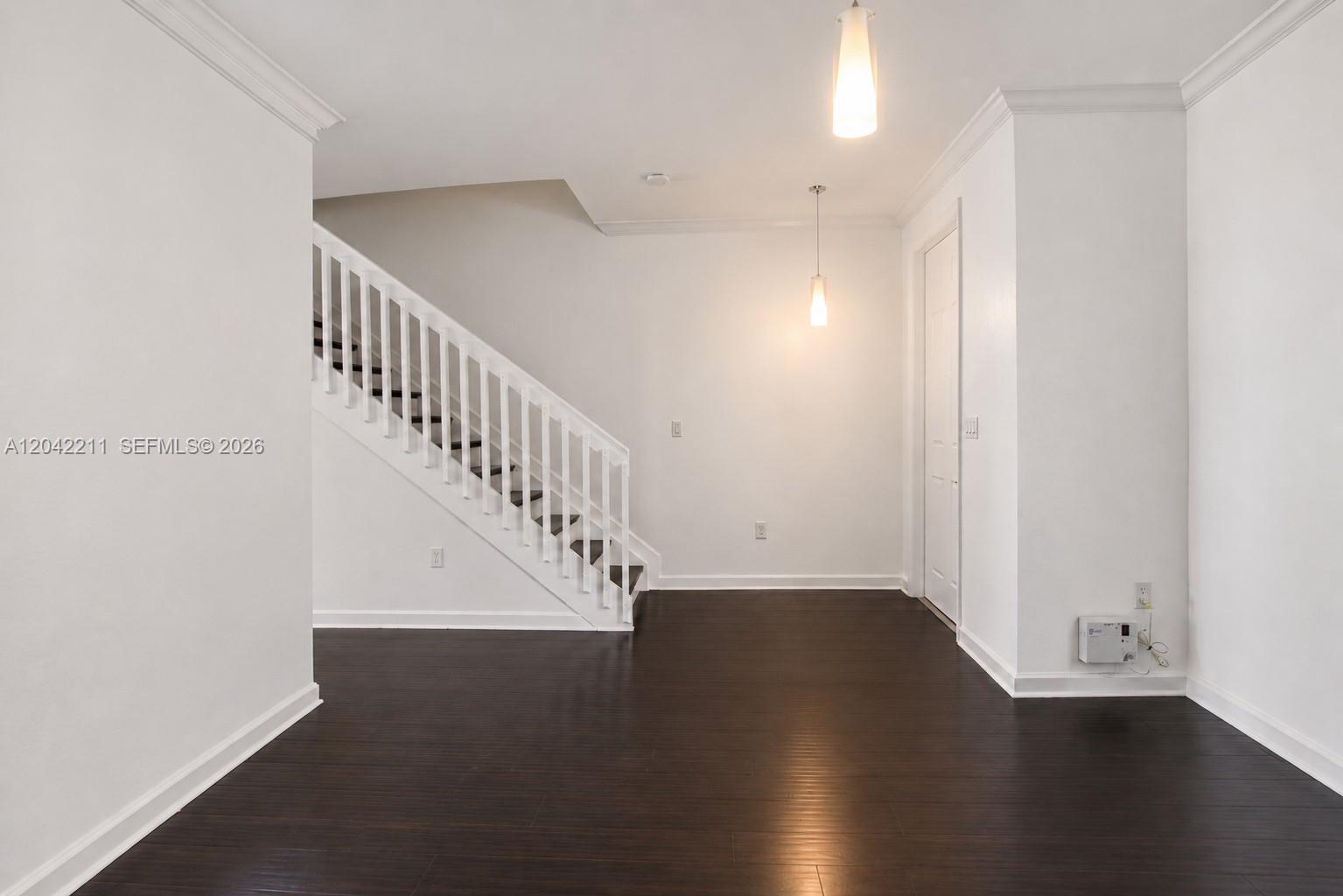 An interior view shows a room with dark wood flooring, white walls, and a staircase — 8954 W 35th Way, Hialeah FL 33018, HIALEAH, FL