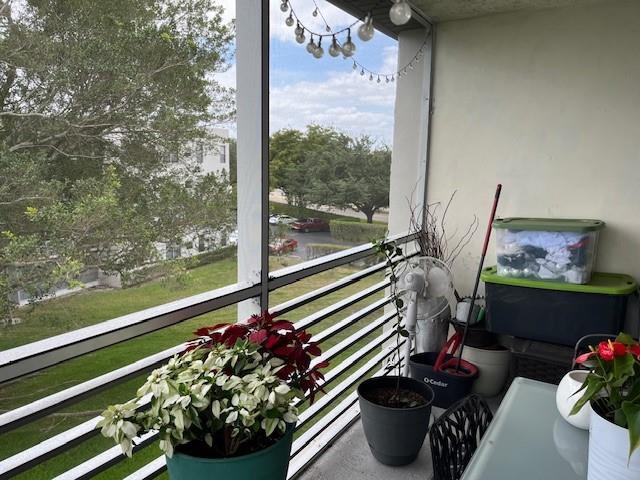 A screened-in balcony features potted plants, storage bins, and a view of trees and parking — 9330 Lagoon Place # 406, Davie FL 33324, DAVIE, FL
