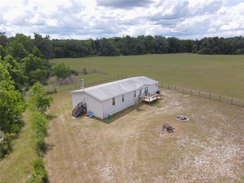 An aerial view shows a single-wide mobile home situated on a large, fenced grassy lot — 11804 SE COUNTY ROAD 234, MICANOPY, FL