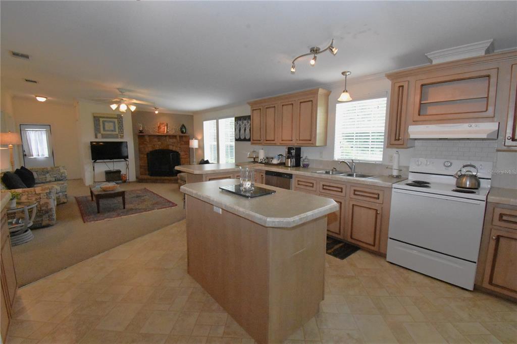 An open-concept kitchen with light wood cabinets and a center island overlooks a living area — 11804 SE COUNTY ROAD 234, MICANOPY, FL