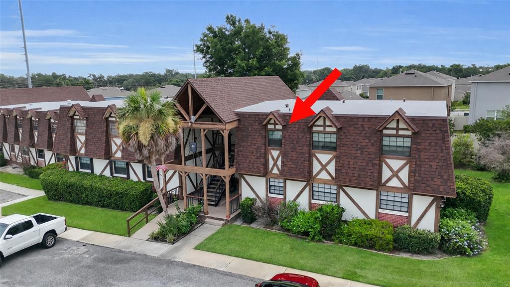 An exterior view of a multi-story apartment building with a red arrow pointing toward a window — 500 NEWELL HILL RD UNIT 110D, LEESBURG, FL