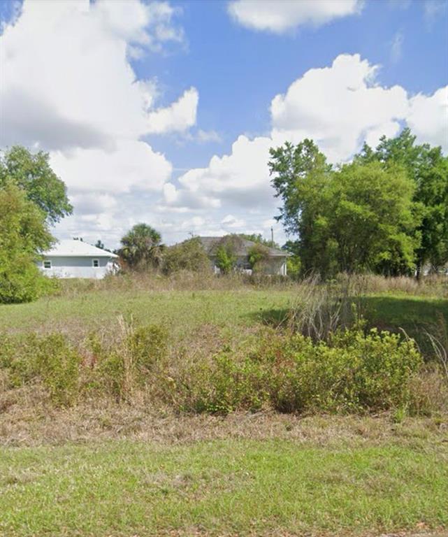 A vacant, grassy lot with scattered shrubs and trees sits in front of two houses — 295 GLENGARY CIRCLE, PUNTA GORDA, FL