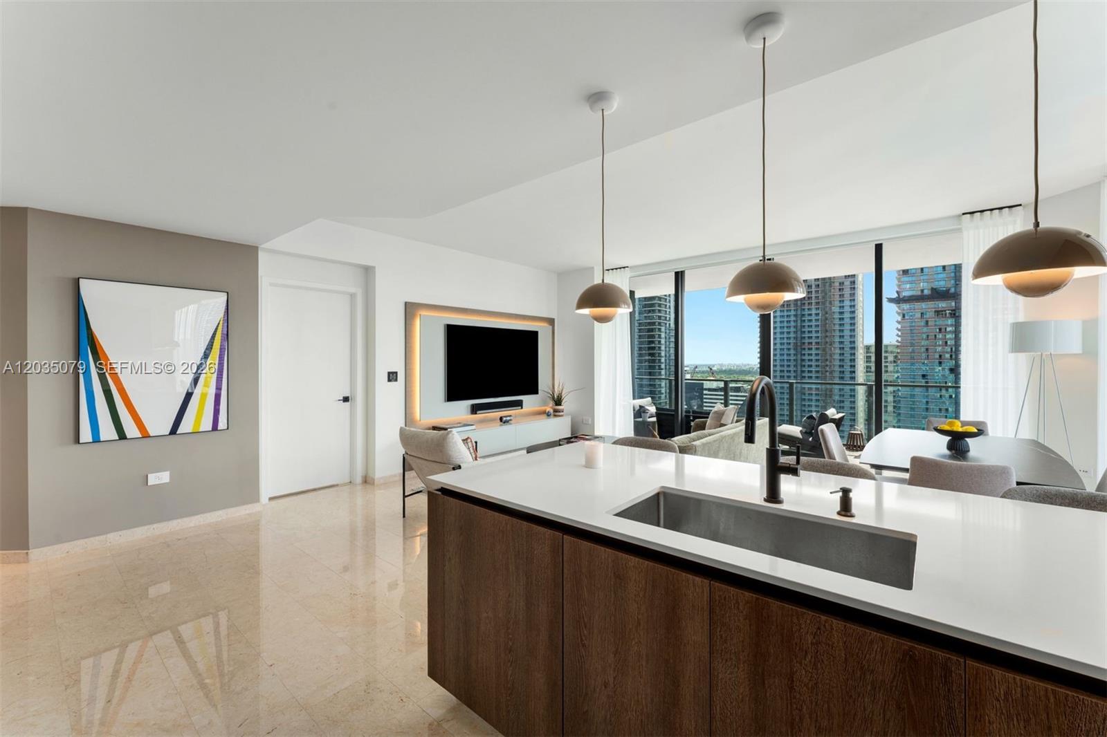 A modern kitchen island with a sink overlooks a living area with floor-to-ceiling windows — 68 SE 6th St # 2612, Miami FL 33131, MIAMI, FL