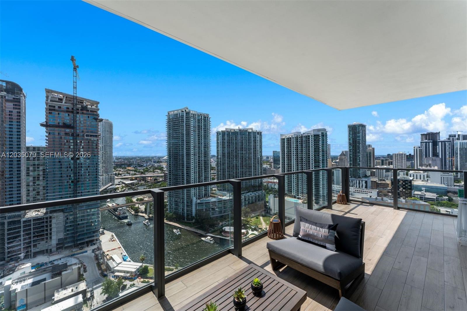 A balcony with wood-look tile flooring overlooks a river and city skyline — 68 SE 6th St # 2612, Miami FL 33131, MIAMI, FL