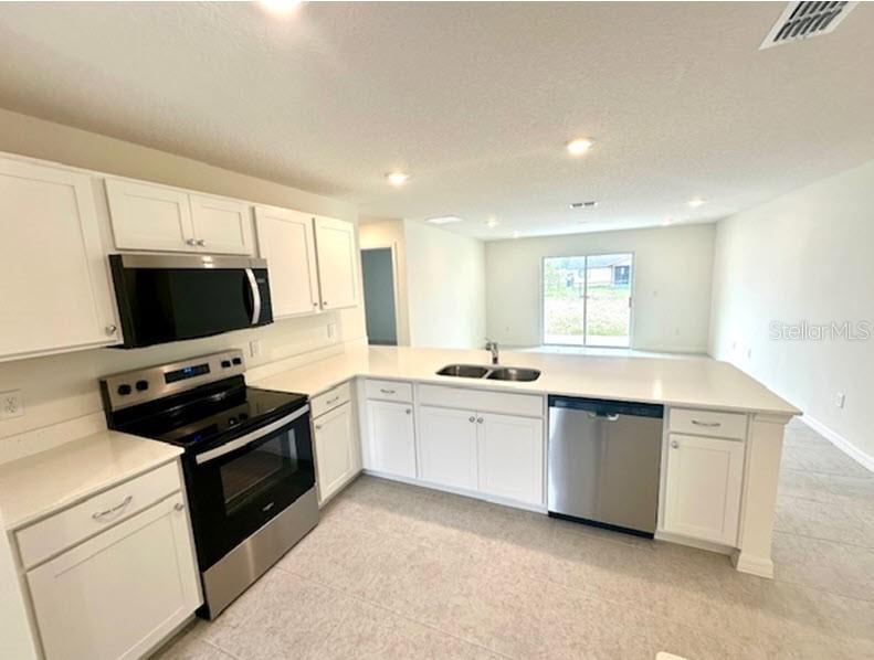 A kitchen features white cabinets, stainless steel appliances, and a peninsula with a sink — 91 BRESSLER LANE, PALM COAST, FL