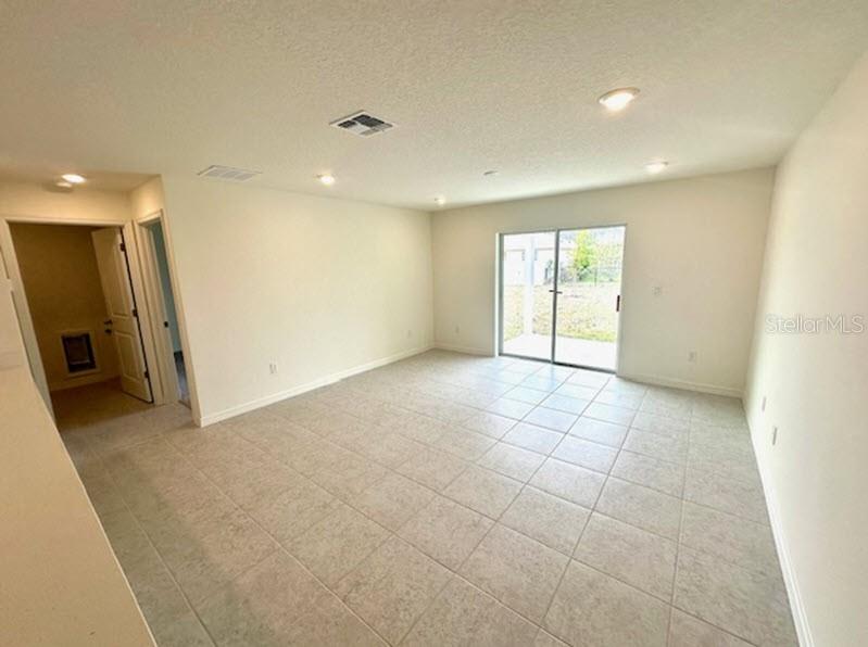 An empty room with light-colored tile flooring, recessed lighting, and sliding glass doors to outside — 91 BRESSLER LANE, PALM COAST, FL