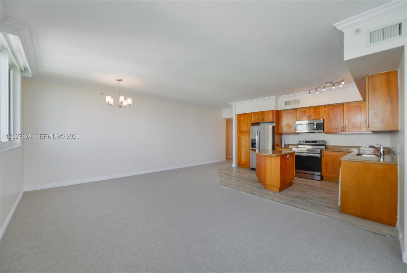 An open-concept living area features carpeted flooring, a dining chandelier, and a wood-cabinet kitchen — 1745 E Hallandale Beach Blvd # 1903W, Hallandale Beach FL 33009, HALLANDALE BEACH, FL
