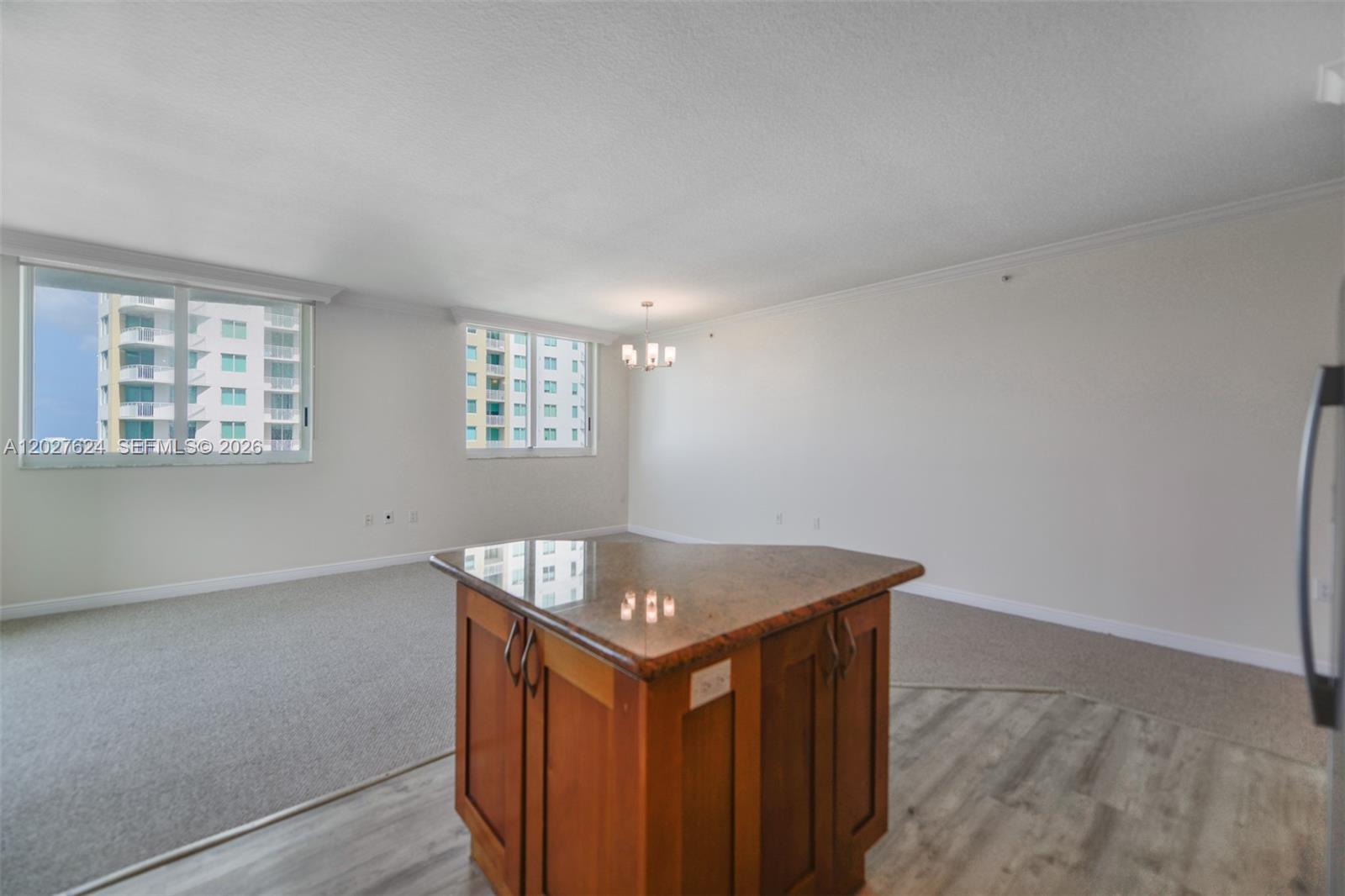 An open living area features a kitchen island with a granite countertop and carpeted flooring — 1745 E Hallandale Beach Blvd # 1903W, Hallandale Beach FL 33009, HALLANDALE BEACH, FL