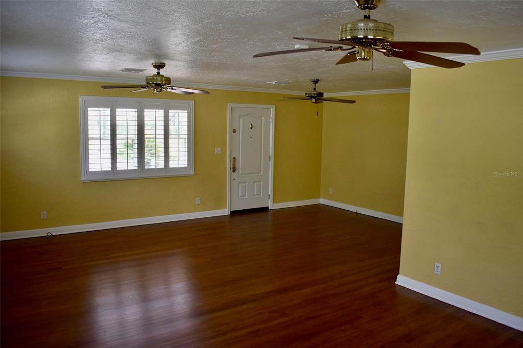 A living room with yellow walls, wood flooring, two ceiling fans, and a white door — 2200 E GORE STREET, ORLANDO, FL