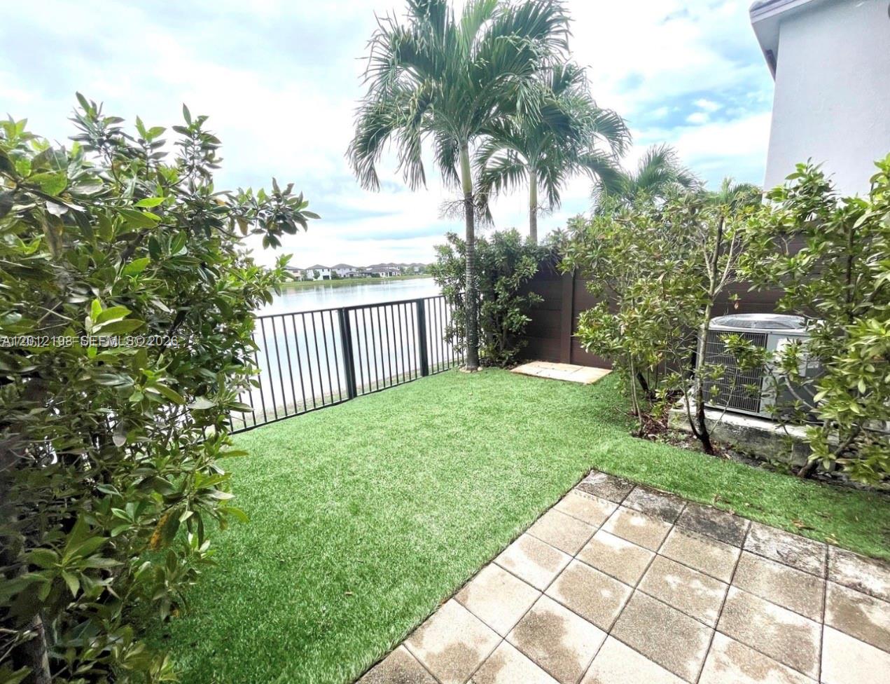 A small backyard features artificial turf, a paved patio, and a metal fence overlooking water — 9083 NW 159th St # 9083, Miami Lakes FL 33018, MIAMI LAKES, FL