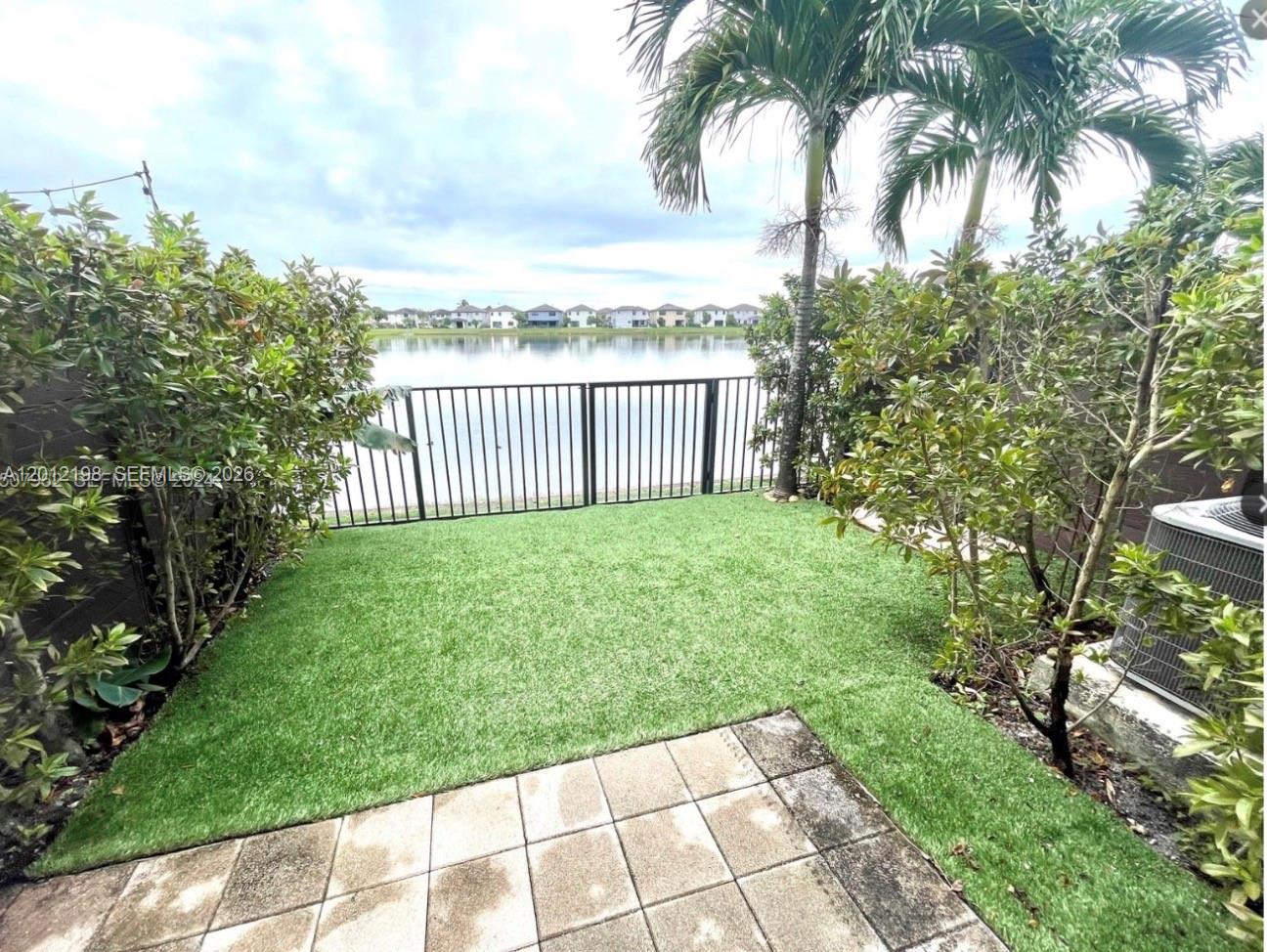 A small backyard with artificial turf, a paved patio, and a black metal fence overlooking a lake — 9083 NW 159th St # 9083, Miami Lakes FL 33018, MIAMI LAKES, FL