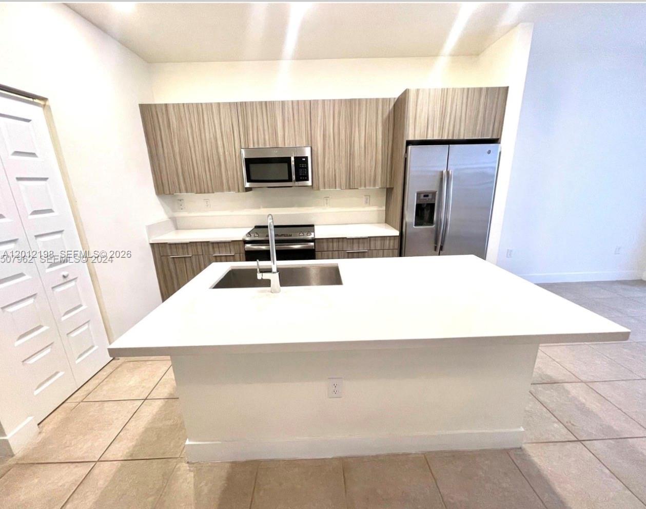 A kitchen features a white island with a sink, stainless steel appliances, and wood-grain cabinets — 9083 NW 159th St # 9083, Miami Lakes FL 33018, MIAMI LAKES, FL
