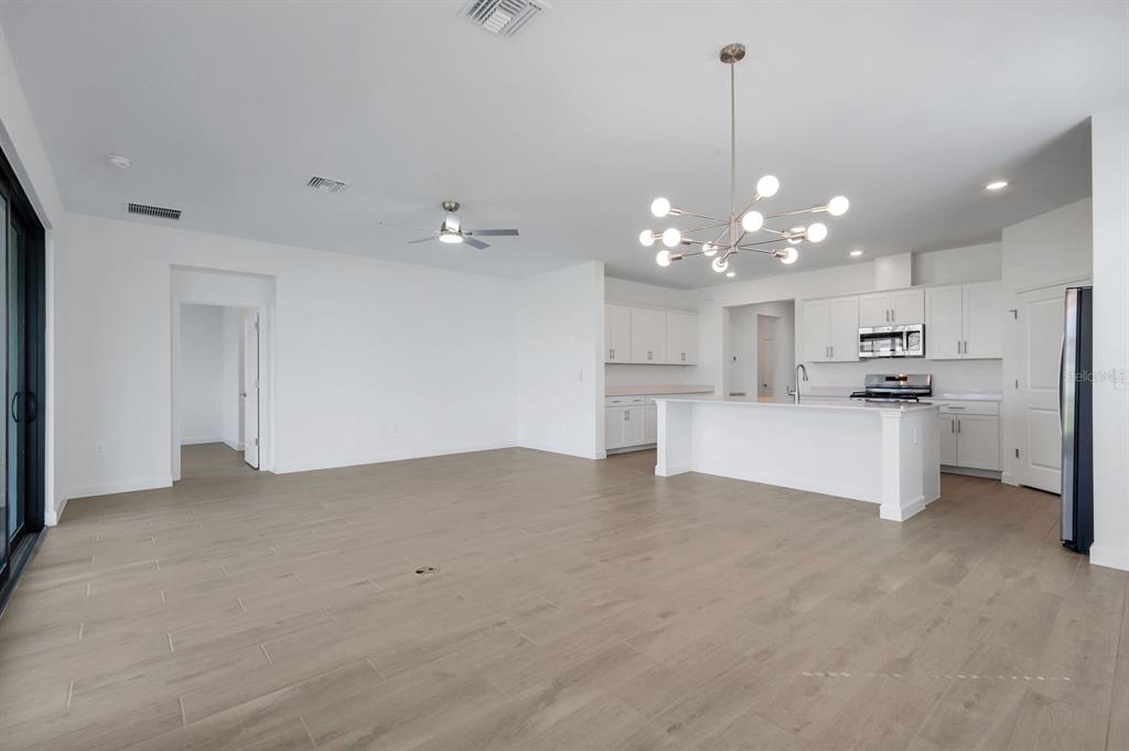 An open-concept kitchen and living area with white cabinets, a central island, and light flooring — 19232 GENTRY PLACE, ESTERO, FL