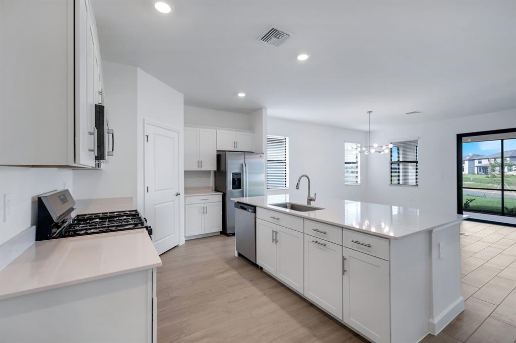 A modern kitchen features white cabinetry, quartz countertops, stainless steel appliances, and light wood flooring — 19232 GENTRY PLACE, ESTERO, FL