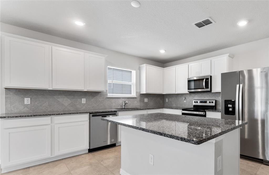 A kitchen with white cabinets, granite countertops, stainless steel appliances, and a central island — 9642 SUMMERS CAY CIRCLE, THONOTOSASSA, FL