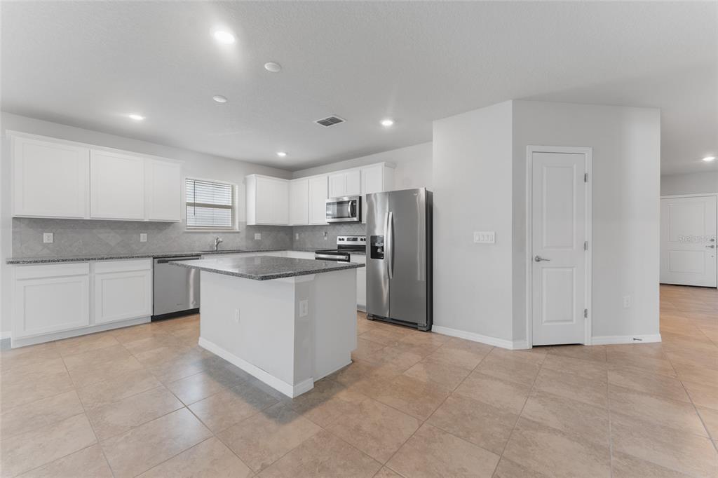 A kitchen with white cabinets, stainless steel appliances, a granite island, and tiled flooring — 9642 SUMMERS CAY CIRCLE, THONOTOSASSA, FL