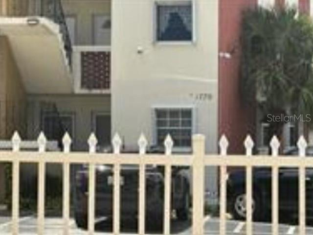 A white multi-story apartment building is viewed through a white picket fence — 1770 79TH ST CAUSEWAY UNIT D111, NORTH BAY VILLAGE, FL