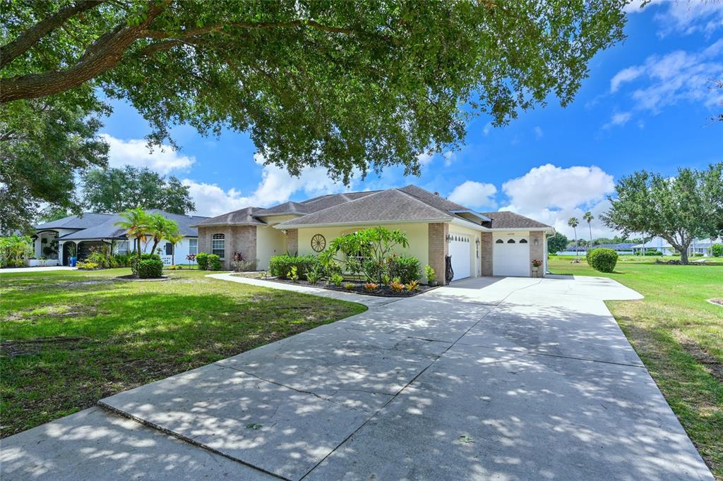 A single-story house with a beige exterior, a concrete driveway, and a large shade tree — 14722 1ST AVENUE E, BRADENTON, FL