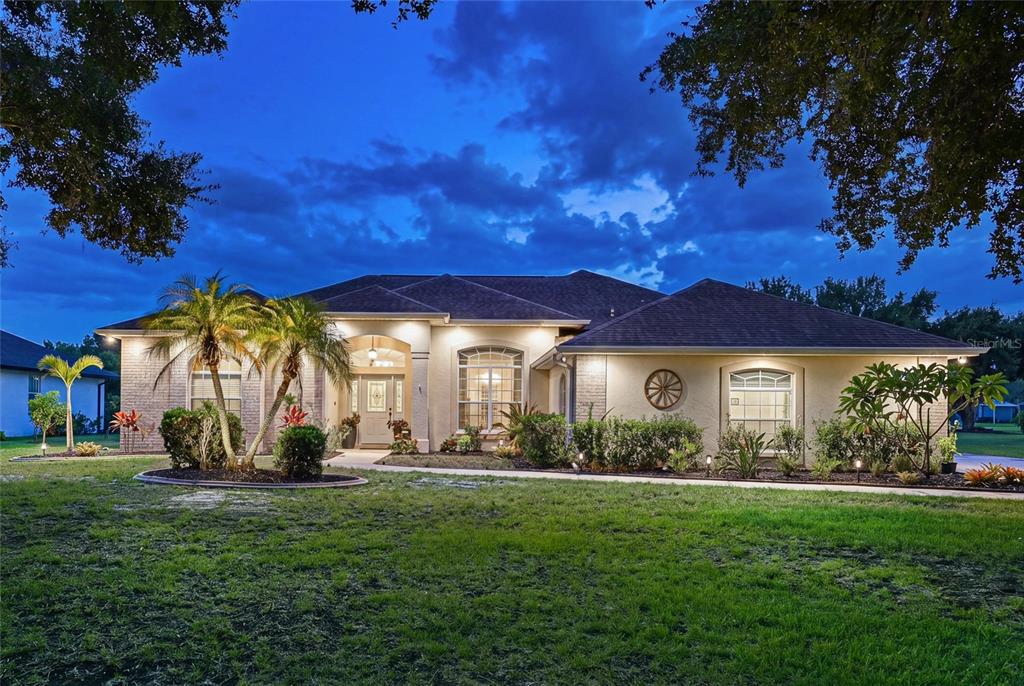 A single-story house with a brick facade, arched windows, and palm trees at dusk — 14722 1ST AVENUE E, BRADENTON, FL