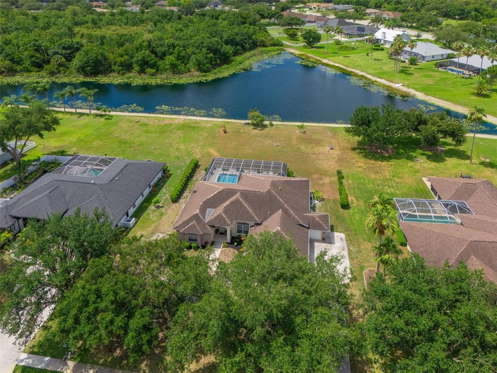 An aerial view shows a house with a pool cage near a pond and trees — 14722 1ST AVENUE E, BRADENTON, FL