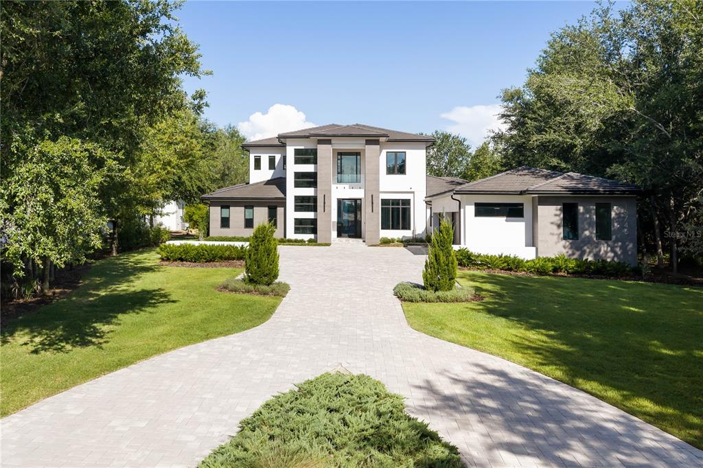 A modern two-story house with a paved driveway and landscaped lawn under a blue sky — 15746 PENDIO DR, MONTVERDE, FL