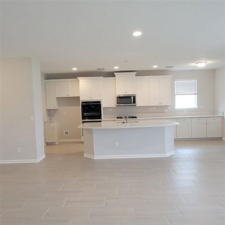 A bright kitchen features white cabinetry, a central island, and light-colored tile flooring — 3399 WOODIE RUN, ORANGE PARK, FL