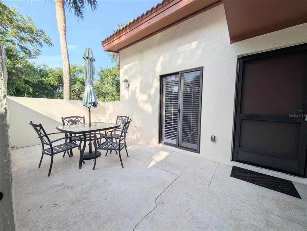 A patio features a glass-topped table with four chairs, a closed umbrella, and sliding doors — 3426 WOOD OWL CIRCLE UNIT 73B, BRADENTON, FL