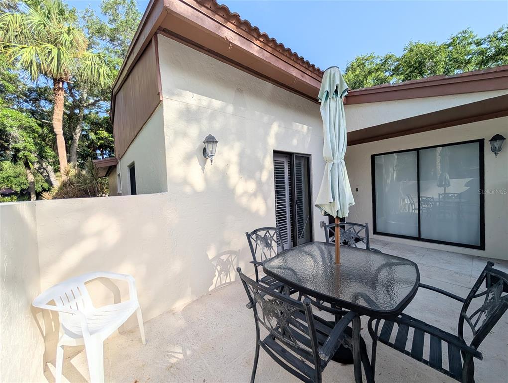 A patio features a glass-topped table with chairs, a closed umbrella, and a white chair — 3426 WOOD OWL CIRCLE UNIT 73B, BRADENTON, FL