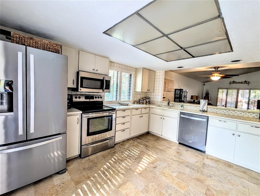 A kitchen features stainless steel appliances, white cabinetry, and light-colored stone tile flooring — 3426 WOOD OWL CIRCLE UNIT 73B, BRADENTON, FL
