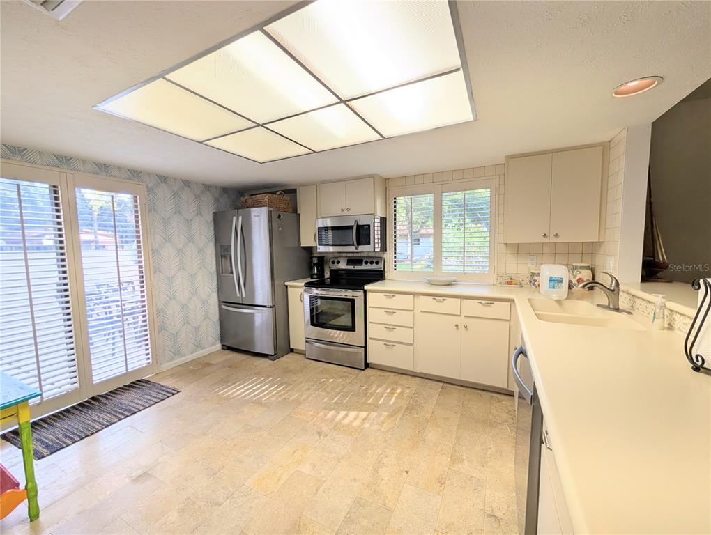 A kitchen features stainless steel appliances, light-colored cabinetry, tile flooring, and a large ceiling light — 3426 WOOD OWL CIRCLE UNIT 73B, BRADENTON, FL