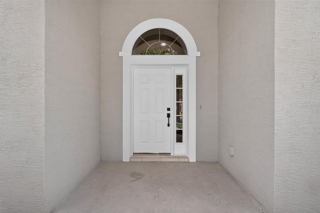 A white front door with a sidelight and arched transom sits in a recessed entryway — 3555 MARIBELLA DRIVE, NEW SMYRNA BEACH, FL