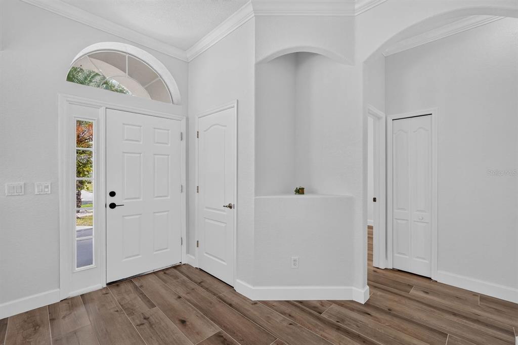 A bright entryway features wood-look tile flooring, a white front door, and a recessed wall niche — 3555 MARIBELLA DRIVE, NEW SMYRNA BEACH, FL