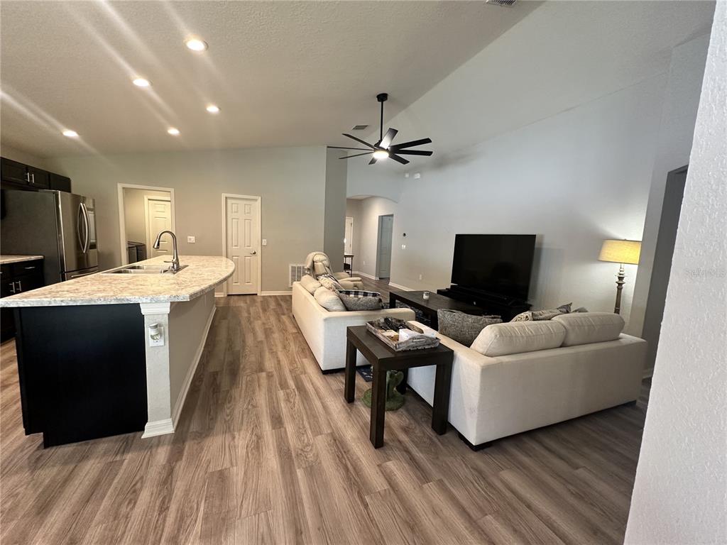 An open-concept living room features a kitchen island, light wood flooring, and a vaulted ceiling — 6911 GIDEON CIR, ZEPHYRHILLS, FL