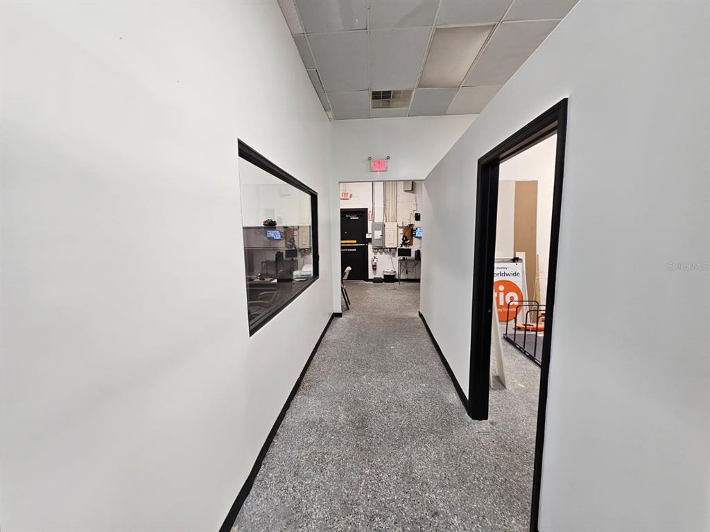 A hallway with white walls, a gray speckled floor, and a window looking into an office — 624 S PINE AVENUE, OCALA, FL
