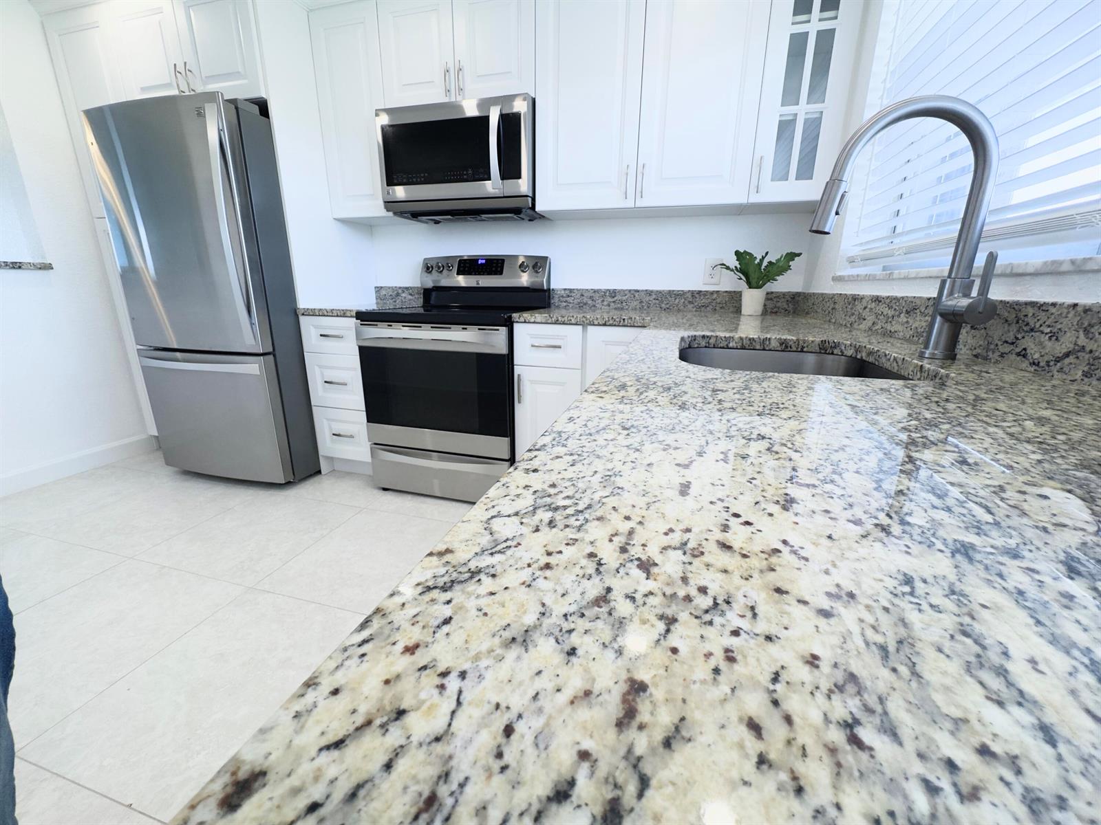 A kitchen features white cabinets, stainless steel appliances, and speckled granite countertops — 2016 S Federal Highway # 404, Boynton Beach FL 33435, BOYNTON BEACH, FL