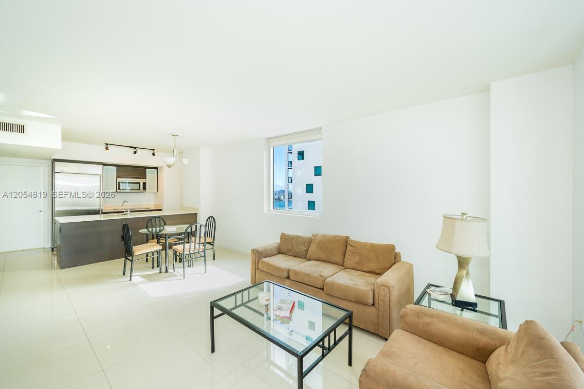 An open-concept living and dining area features white tile floors, a kitchen island, and furniture — 55 SE 6 STREET # 2210, Miami FL 33131, MIAMI, FL