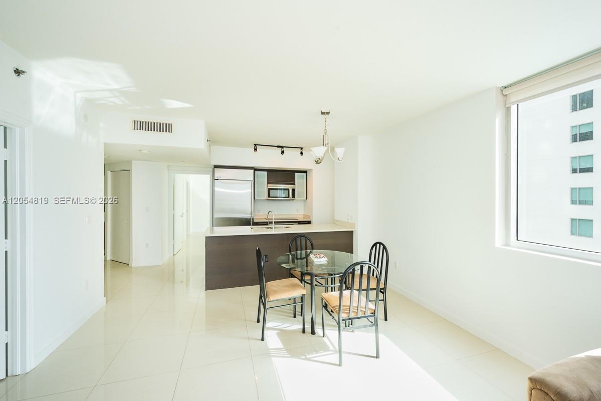 A modern kitchen with stainless steel appliances overlooks a dining area with a glass table — 55 SE 6 STREET # 2210, Miami FL 33131, MIAMI, FL