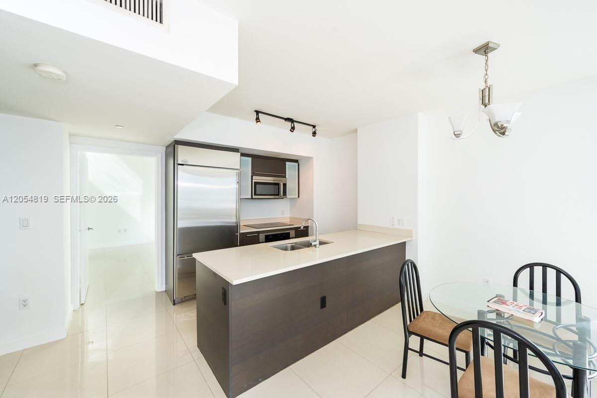 A modern kitchen features dark cabinetry, stainless steel appliances, and a central island with seating — 55 SE 6 STREET # 2210, Miami FL 33131, MIAMI, FL