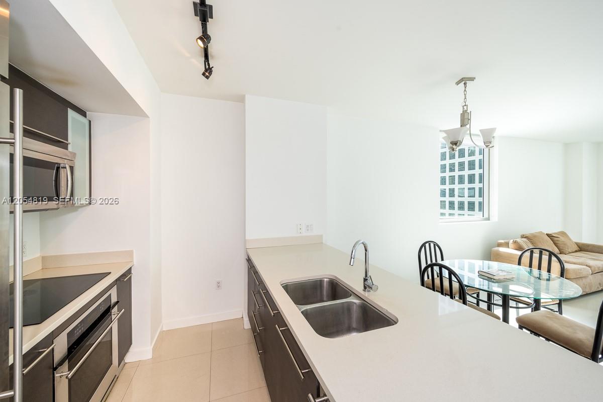 A modern kitchen features dark cabinetry, light countertops, a double sink, and a dining area — 55 SE 6 STREET # 2210, Miami FL 33131, MIAMI, FL