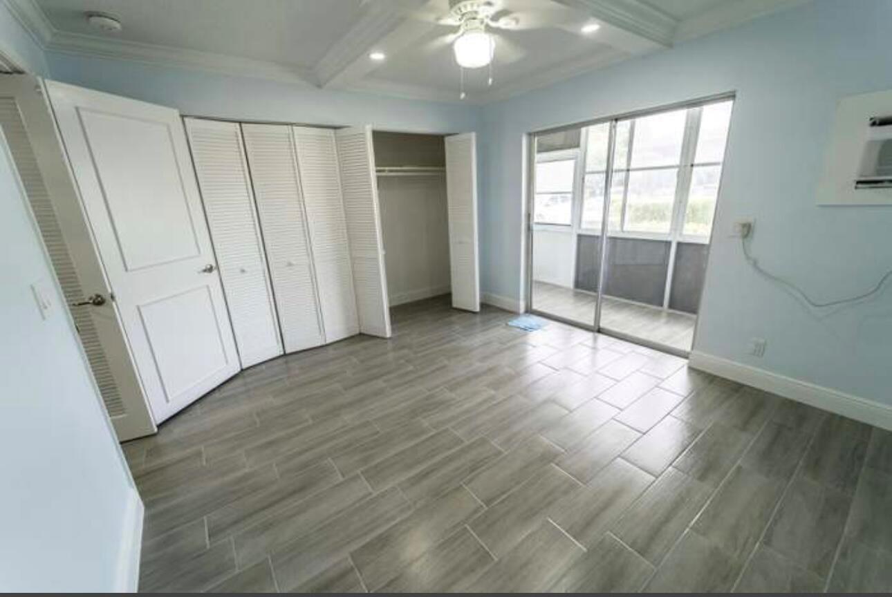An empty bedroom with gray wood-look tile flooring, a white closet, and a sliding glass door — 309 Windsor N, West Palm Beach FL 33417, WEST PALM BEACH, FL