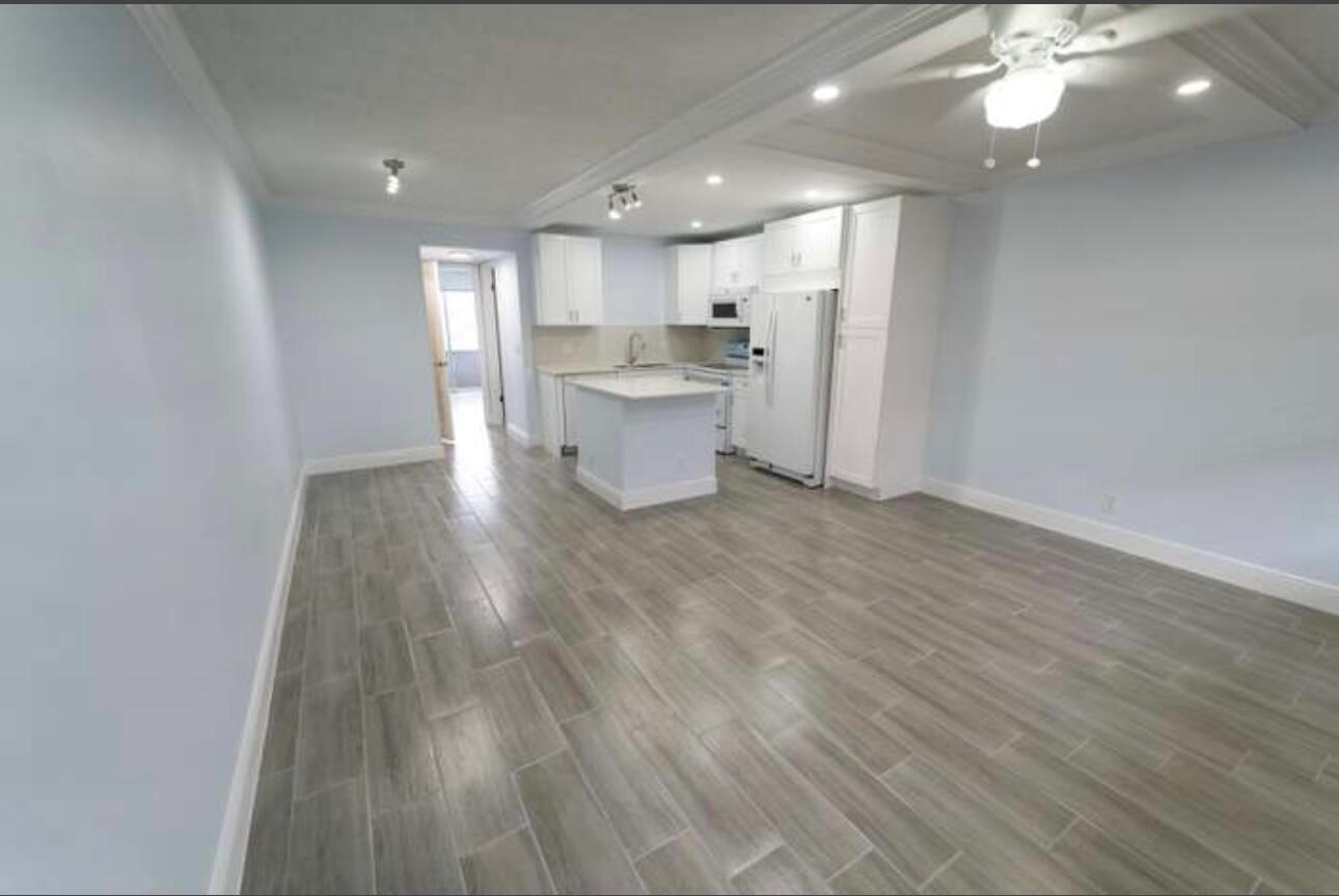 An open-concept kitchen and living area featuring white cabinetry, a center island, and wood-look flooring — 309 Windsor N, West Palm Beach FL 33417, WEST PALM BEACH, FL