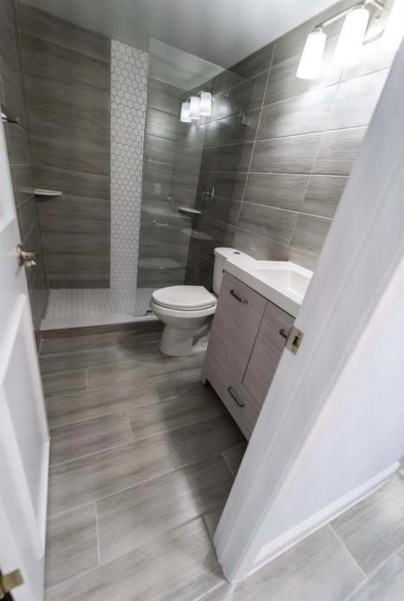 A modern bathroom features gray wood-look tile flooring, a glass-enclosed shower, and a vanity — 309 Windsor N, West Palm Beach FL 33417, WEST PALM BEACH, FL