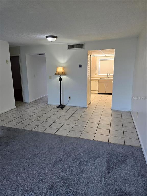 A room with gray carpet and white tile flooring leads to a kitchen doorway — 712 OAKGROVE DRIVE UNIT 230, BRANDON, FL