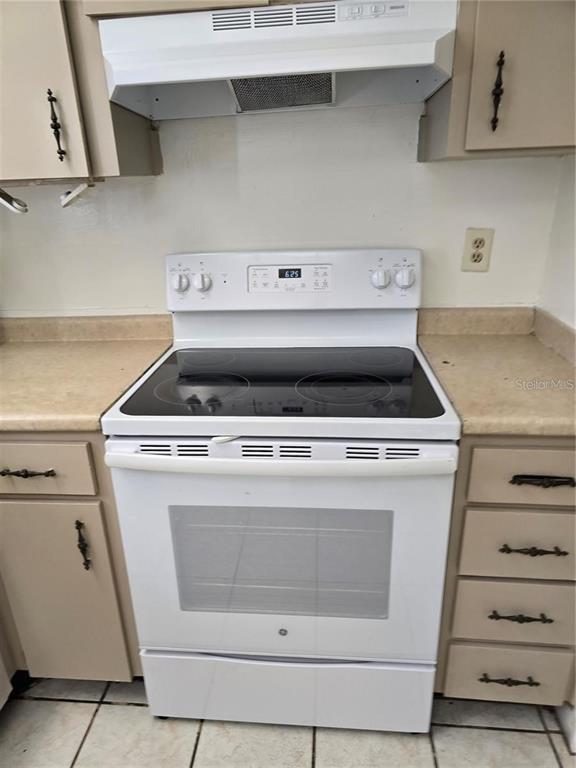 A white electric range sits between beige cabinets and a tan countertop in a kitchen — 712 OAKGROVE DRIVE UNIT 230, BRANDON, FL