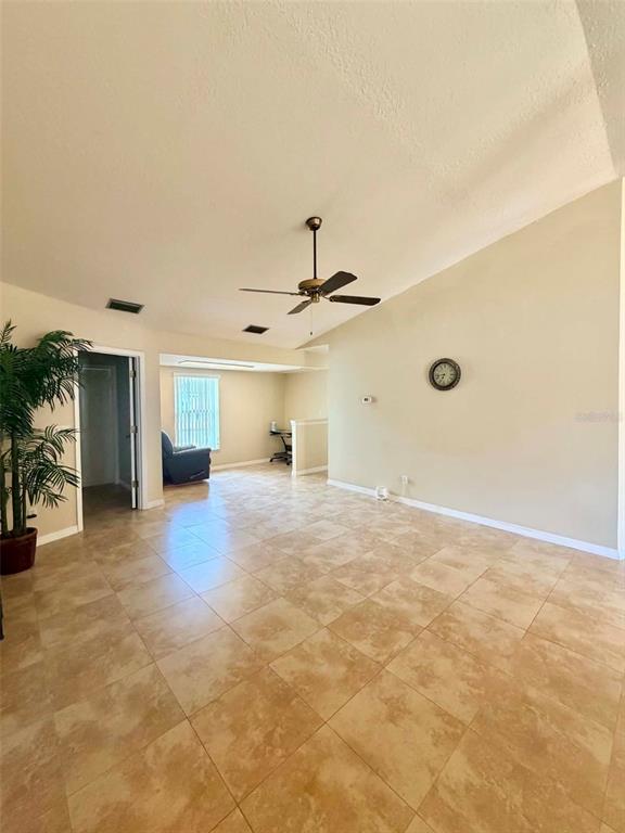 A living room with vaulted ceilings, tile flooring, a ceiling fan, and a wall clock — 5647 DALTON COURT, NEW PORT RICHEY, FL