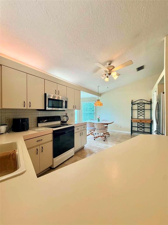 A kitchen with beige cabinets, white countertops, and a dining area in the background — 5647 DALTON COURT, NEW PORT RICHEY, FL