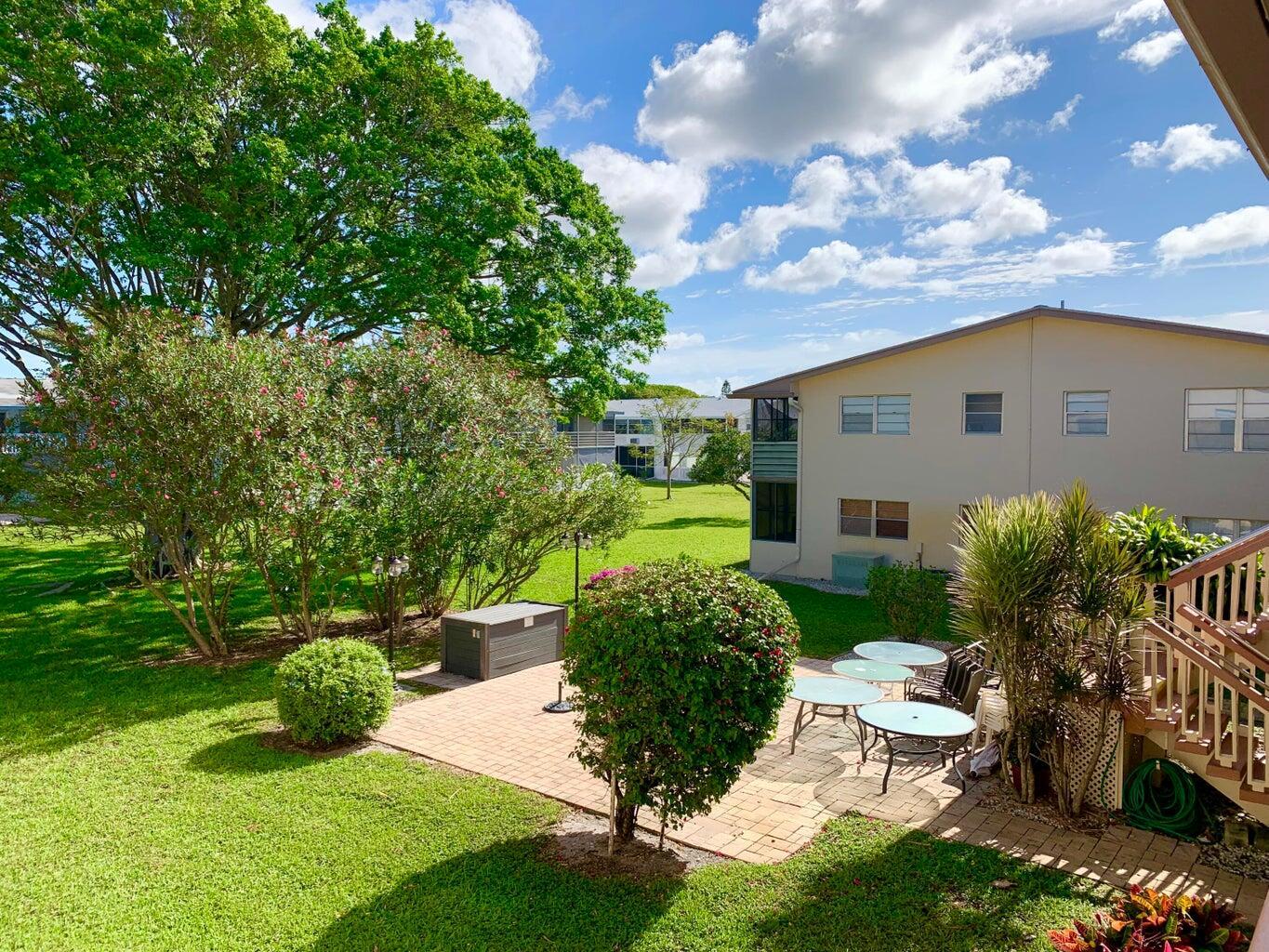A patio with outdoor furniture sits on a grassy lawn beside a multi-story apartment building — 116 Canterbury E, West Palm Beach FL 33417, WEST PALM BEACH, FL