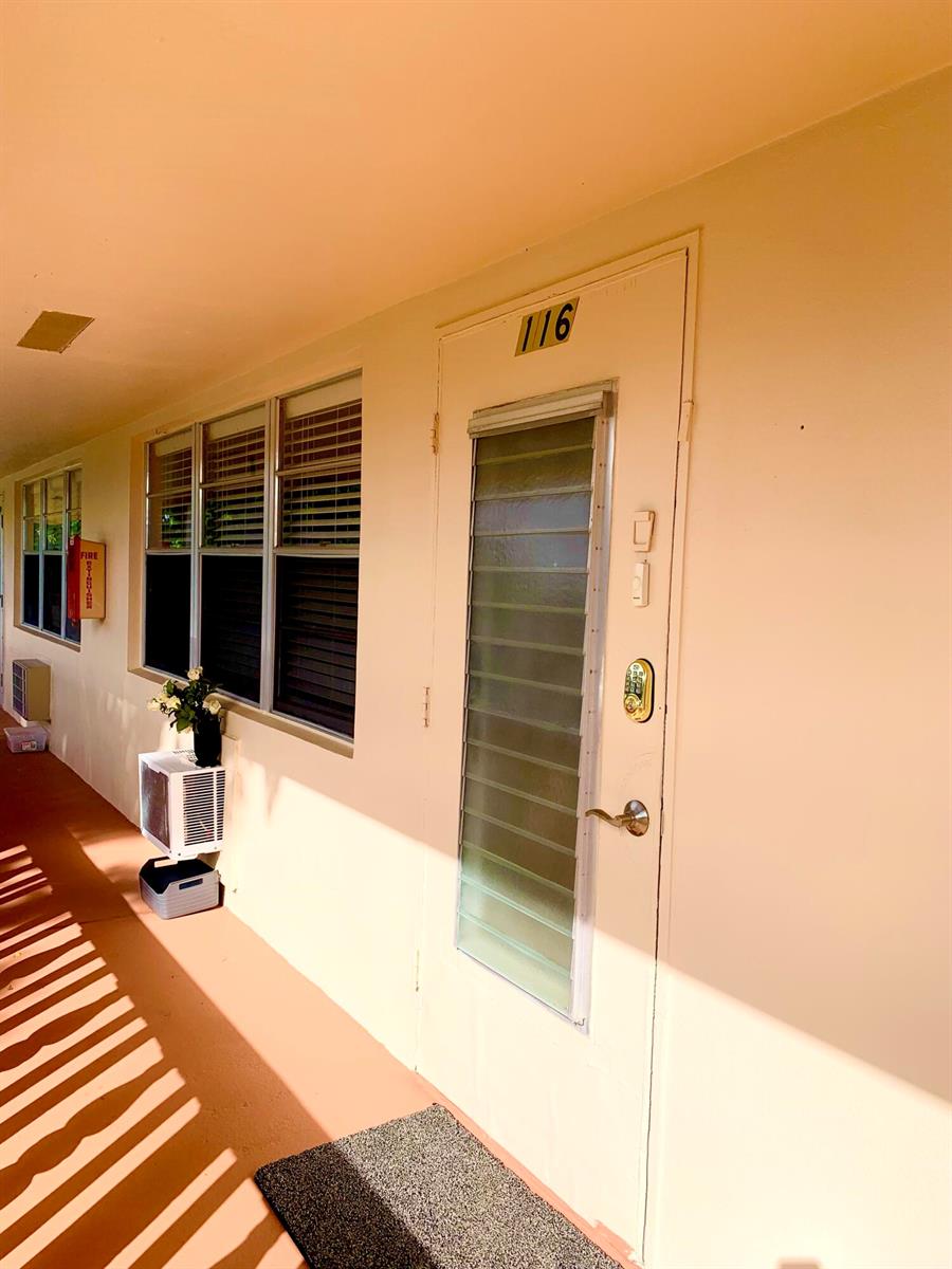 An exterior view of a building hallway showing a door numbered 116 and windows — 116 Canterbury E, West Palm Beach FL 33417, WEST PALM BEACH, FL