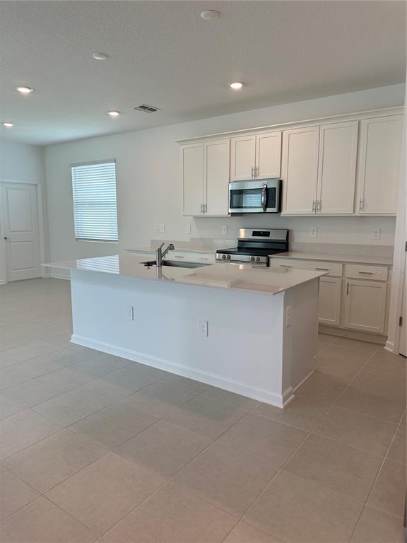 A kitchen features white cabinets, a central island with a sink, and a gray backsplash — 2981 GOOD VIBES WAY, CLERMONT, FL