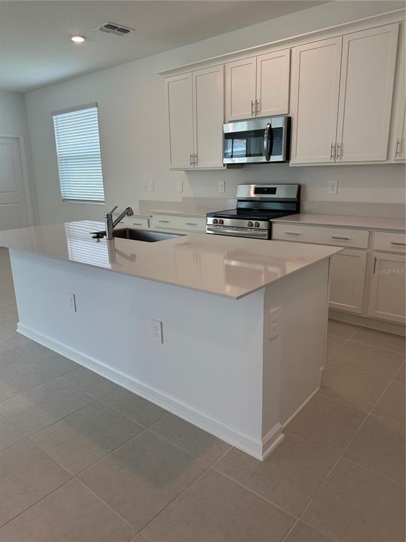 A modern kitchen features white cabinetry, a central island, stainless steel appliances, and tile flooring — 2981 GOOD VIBES WAY, CLERMONT, FL